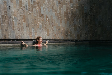 Woman Swimming Alone in Modern Luxury Pool. Minimalist Travel Escape with Calm Water and Textured Stone Wall