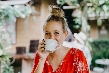 Smiling Woman Drinking Coffee in Tropical Outdoor Café – Joyful Lifestyle Moment with Relaxed...
