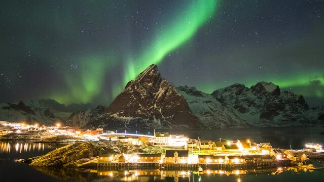 Time lapse of aurora borealis dancing on mountains with fishing village.