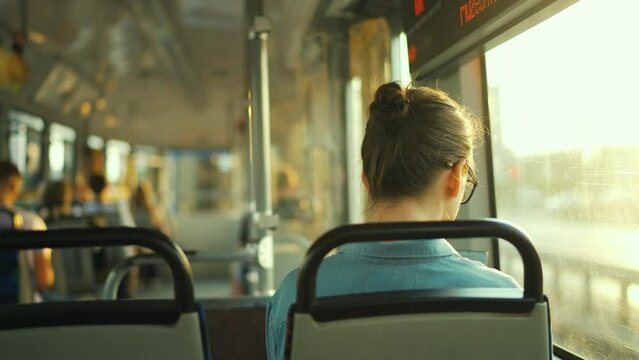 Woman in tram using smartphone chatting and texting with friends, back view. City, urban, transportation. Slow motion