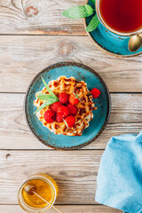Stack of belgian waffles with honey, mint and fresh raspberries on turqouise plate