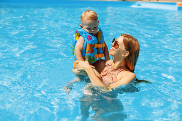 mother and her little son an adorable laughing boy having fun together in an outdoor swimming pool on a hot summer day