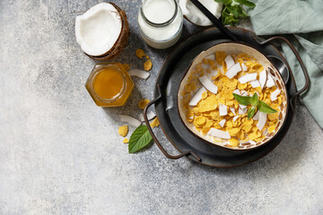 Summer vegan breakfast. Cereal granola breakfast flakes with coconut non-dairy alternative milk and fresh coconut slices on a stone tabletop. View from above. Copy space.