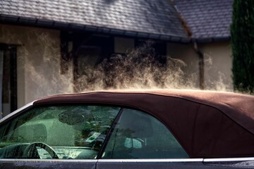 Closeup of car with evaporating steam on roof the background of house under morning rays of the sun
