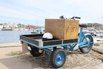 Blue Utility moped parked on a stone wharf. Coastal village, boats and sea in background