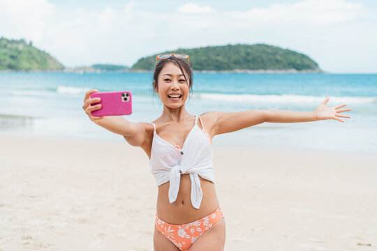 Portrait of happy smiling beautiful women taking a selfie photo on the beach. Pretty young Asian girl in casual looking clothes recording vlog video in bright sky