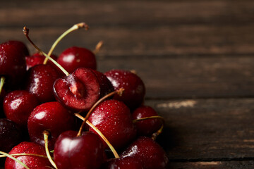 Close up of pile of sweet red cherries with stalks and leaves on a wooden table. Black background. Food and fruit concept. Space for your text