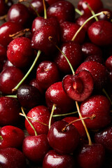 Close up of pile of sweet red cherries with stalks and leaves. Large collection of fresh red cherries. Ripe cherries background. Food and fruit concept