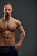 Obraz premium Croped shot of Young male athlete posing. Handsome athletic male power guy. Fitness muscular person. Young athlete showing muscles in the studio, posing shirtless on gray background.