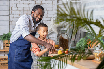 Black father and his son kid cooking fresh vegetables on kitchen at home. African dad and boy child preparing together.