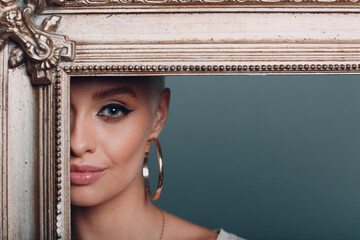 Millenial young woman with short blonde hair holds gilded picture frame. Museum restoration...