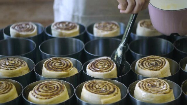 Softened butter being brushed onto freshly cut raw cinnamon roll dough placed in oven tray, prepared for over, filmed as close up