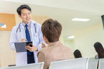 Fototapeta premium A handsome young Asian doctor in Thailand discussing the symptoms of a female patient attending the hospital.