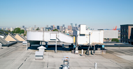 Hvac unit on flat roof with downtown skyline, vents and rooftop hatches and blue sky. Rooftop...