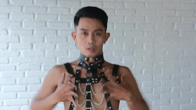 Sexy transgender sensually shows his inner essence in an expressive dance. The bisexual model is dressed in leather clothes with belts and chains for BDSM. Male Asian gay model with earrings.
