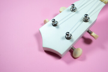 Close up neck of the guitar..White colored wooden ukulele guitar on the pink background. Hawaiian Four String Guitar. Musical Instrument.