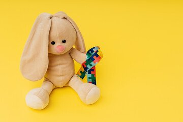 World autism awareness and pride day. Puzzle pattern ribbon and toy bunny on a yellow background