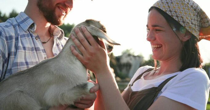 Couple of young man and girl, spending holiday on farm and playing with goat