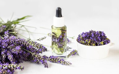 Obraz na płótnie Canvas Glass bottle of Lavender essential oil with fresh lavender flowers and dried lavender seeds on white background, aromatherapy spa massage concept. Lavandula oleum.