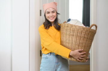 Young happy woman wearing yellow shirt holding a basket full of clothes at home, laundry concept