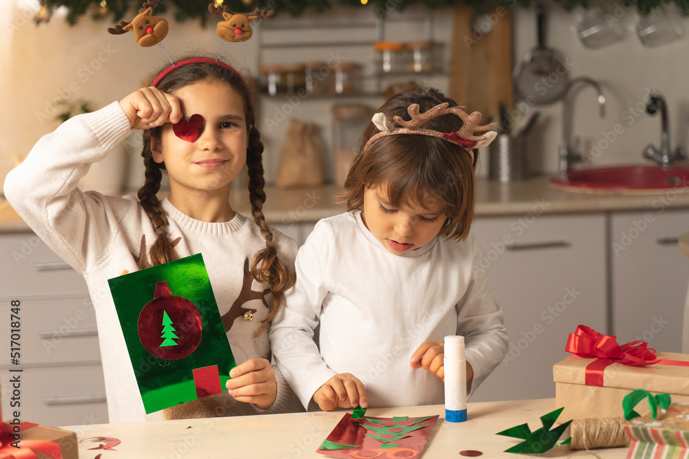 Wall mural cheerful kids make a christmas card for mom. funny sisters prepare for christmas and new year at hom