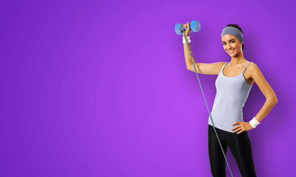 Happy smiling african american woman doing exercise with growth and dumbbell, isolated on violet purple background. Young sporty model at studio. Health, beauty and fitness concept.