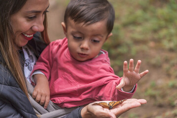 Baby boy trying to grab a monarch butterfly on his mom's hand