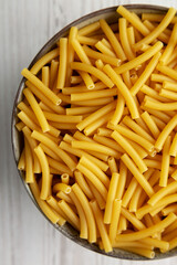 Dry Organic Maccheroni Pasta in a Bowl on a white wooden surface, top view. Flat lay, overhead, from above. Close-up.