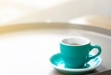 Cup of black hot coffee on a table in cafe with steam and morning sunlight.