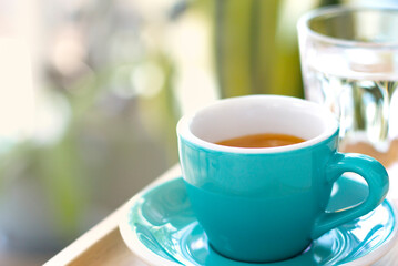 Cup of black hot coffee on a table in cafe with steam and morning sunlight.
