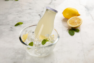 A bottle of healthy Lemon and Mint Juice served in iced cube bowl side view on grey background