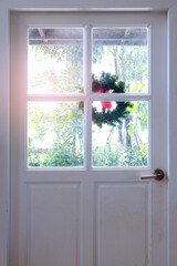 White wood door with glass window design and a flower crown decorated at the outside side to the green garden