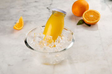 A bottle of FRESH ORANGE JUICE served in iced cube bowl side view on grey background