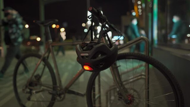 A bicycle parked in the bike parking lot at night near a supermarket. Cycle with helmet and blinker on handlebars parked outside a mall at night. 