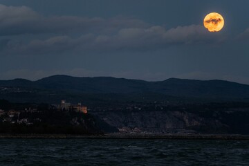 View of the full moon rising above the sea, with castle and coast