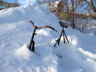 Close-up of old rusty bicycle buried in thick layer of snow in Finnish Lapland. Snowy landscape and extreme nature.