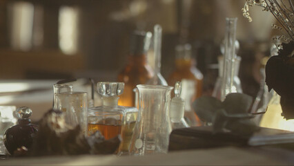 Close-up of a perfumer's workplace. Vintage cinematic concept. Sunny day in the working workshop. Lots of ingredients, a book, glass flasks on the table. Depth of field
