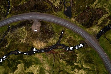 Aerial shot of a white car parked near a curved road surrounded by beautiful nature