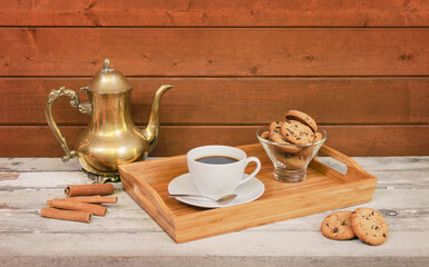 Coffee pot, coffee cup and delicious chocolate chip cookies on wooden tray on aged wooden table.