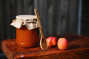 Close-up. Still life. Jar of homemade jam, ripe ready-to-eat red sunny apricots and wooden spoon on rustic wood surface