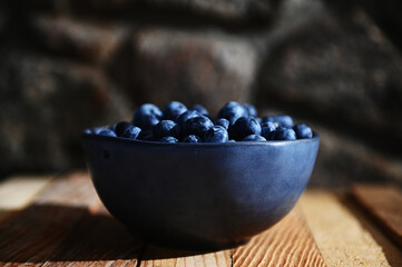 Still life. Close-up. Blue bowl of fresh wild blueberries from an organic farm on rustic wood crate and stone background