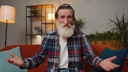 POV of senior grandfather man wearing headset, freelance worker, call center or support service operator helpline, having talk with client or colleague communication support waving hello alone at home