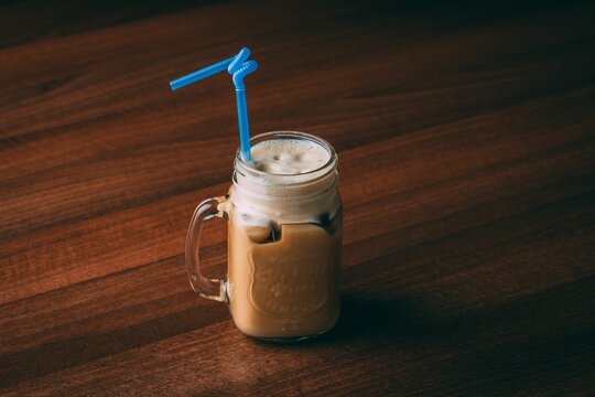 Closeup Shot Of A Frappuccino Coffee In A Glass Cup With A Blue Straw On A Wooden Table