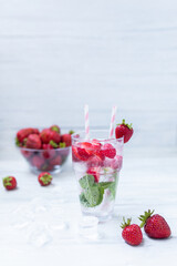 Water with strawberry. Fresh strawberry cocktail. Summer cocktail with strawberry, ice cubes and mint.  Glass of strawberry soda drink on white wooden background.