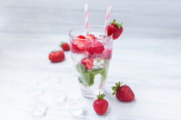 Water with strawberry. Fresh strawberry cocktail. Summer cocktail with strawberry, ice cubes and mint.  Glass of strawberry soda drink on white wooden background.