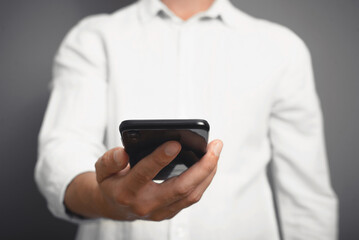 Businessman in white shirt holding mobile phone, indoors. Front view of caucasian man using smartphone, close-up. Selective focus on gadget