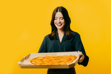 Beautiful young woman with pizza posing on a yellow background.