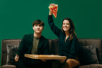 Friends peeing with pizza on the sofa. Studio photo on a green background, mockup.