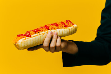 Hot dog in hand close-up. Studio photo on a colored background, copy space.