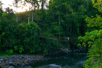 Indonesian scenery with a bridge over the river with two mothers going to the garden